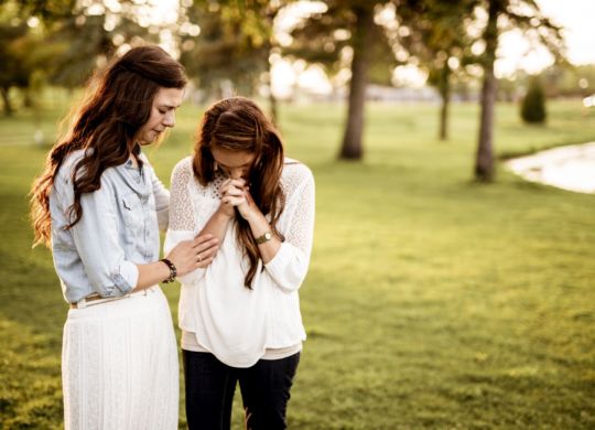 A closeup shot of two female praying with a blurred background